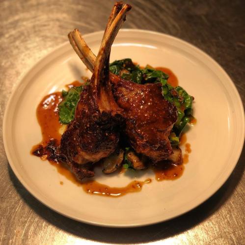 A plate of grilled lamb chops with a rich sauce, served on a bed of sautéed greens and vegetables.