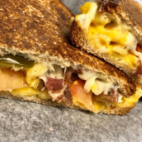 Close-up of a toasted sandwich filled with melted cheese, bacon, vegetables, and creamy sauce, cut in half.