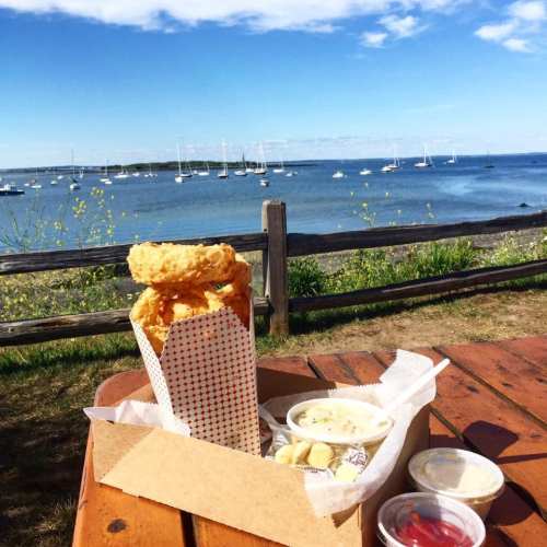 A scenic view of a harbor with sailboats, featuring a meal of fried food and dipping sauces on a wooden table.