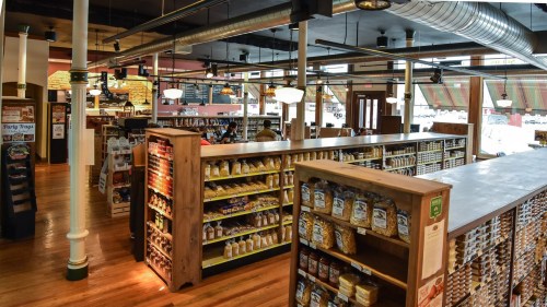 A spacious grocery store interior with wooden shelves stocked with various products and customers shopping.