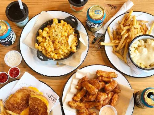 A spread of comfort food including mac and cheese, fries, chicken wings, and drinks on a wooden table.