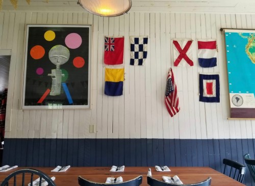 A restaurant wall featuring colorful flags, a framed artwork, and a wooden table set with napkins.