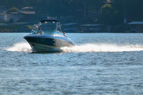 A speedboat glides across a calm lake, leaving a spray of water in its wake on a sunny day.