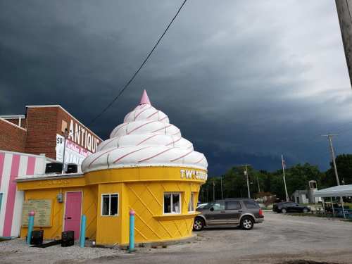 A whimsical ice cream shop shaped like a giant cone, set against a dark, stormy sky.