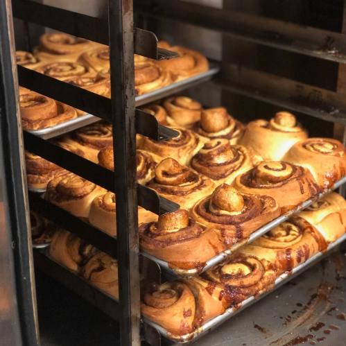 Freshly baked cinnamon rolls on trays in an oven, golden brown and steaming.