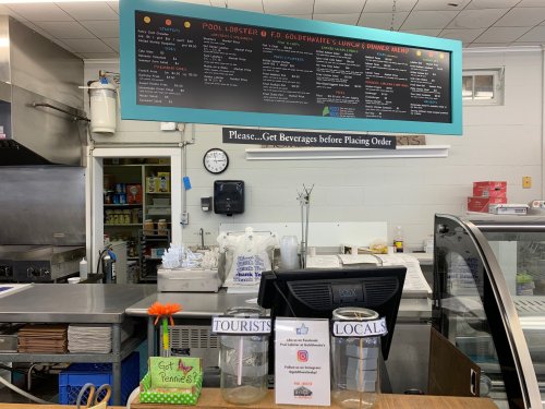 A restaurant counter with a menu board above, two jars labeled "Tourists" and "Locals," and a flower decoration.