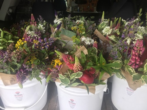 Baskets filled with colorful wildflowers and greenery arranged in white buckets inside a vehicle.
