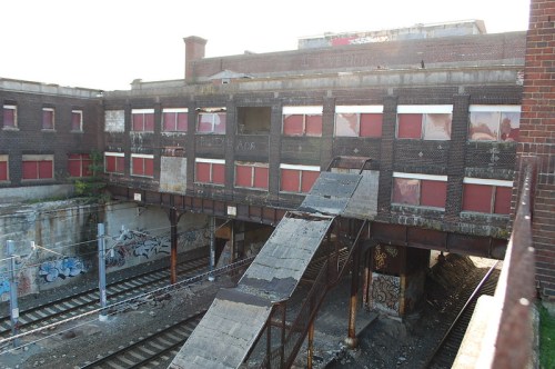 Abandoned building with boarded windows, graffiti, and a sloped ramp leading to train tracks below.
