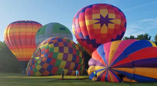 Colorful hot air balloons on the ground, ready for flight, set against a clear blue sky.