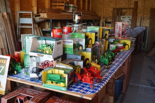 A table filled with various toy tractors and farm equipment models, surrounded by wooden shelves and boxes.