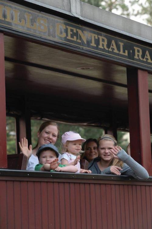 A group of children and adults wave from a train car, smiling and enjoying a ride together.