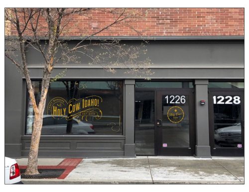Exterior of a storefront with "Holy Cow Idaho!" signage, featuring a tree and parked car in front.