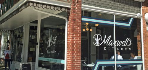 Exterior view of Maxwell's Kitchen, featuring large windows and a modern sign, with diners visible inside.