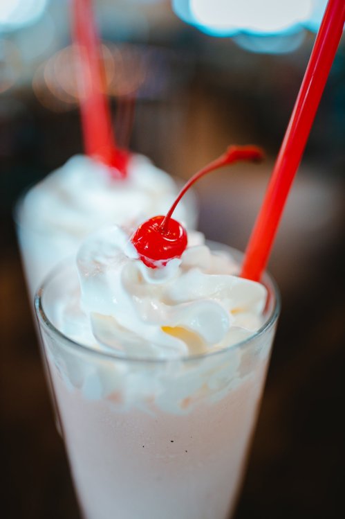Two milkshakes topped with whipped cream and cherries, served in clear glasses with red straws.