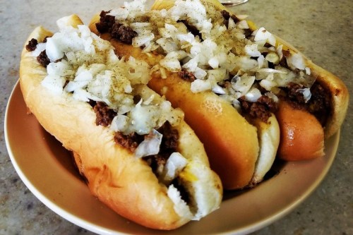 Three hot dogs topped with chopped onions on a plate.