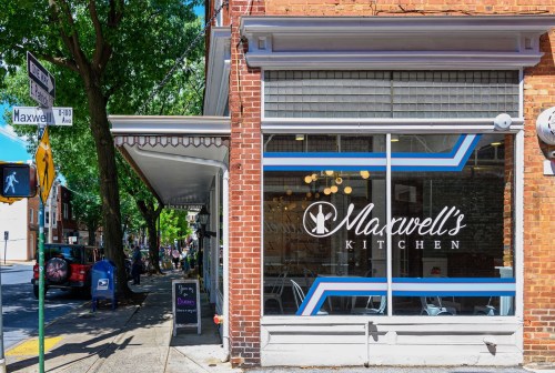 Exterior view of Maxwell's Kitchen, featuring large windows and a brick facade, with trees lining the street.