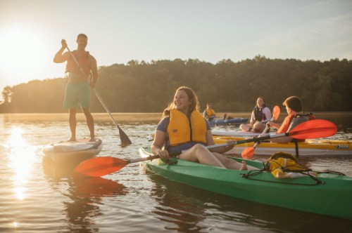 A group of people kayaking on a calm lake during sunset, enjoying the outdoors and each other's company.