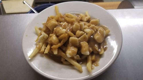A plate of poutine featuring fries topped with cheese curds and brown gravy.