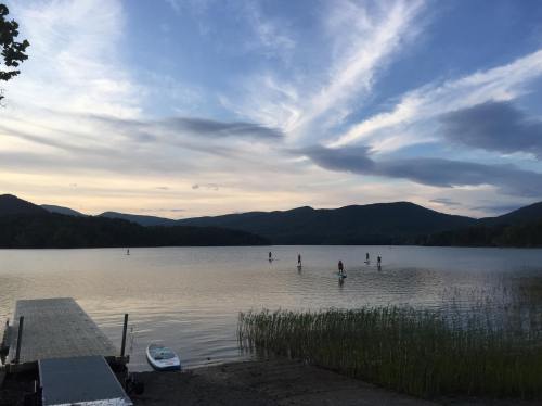 A serene lake at sunset with paddleboarders, mountains in the background, and a wooden dock in the foreground.