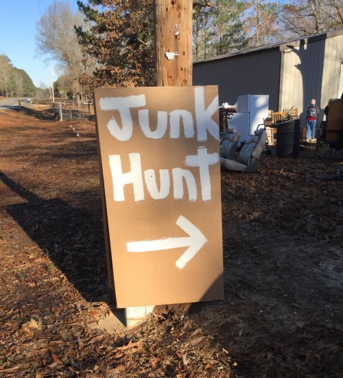 A cardboard sign reading "Junk Hunt" with an arrow pointing to the right, placed near a rural road.