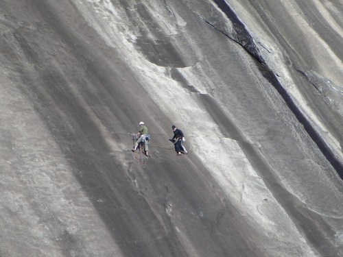 Two climbers ascend a steep, rocky surface, showcasing their skills against a rugged backdrop.