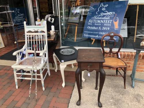 A display of vintage furniture outside a shop, including chairs and tables, with a festival sign in the background.