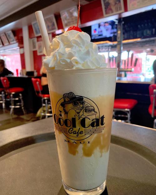 A tall glass of creamy dessert topped with whipped cream and a cherry, featuring the Cool Cat Cafe logo.