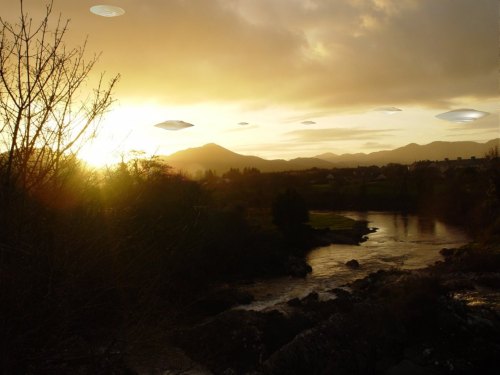 A sunset over a river with mountains in the background, featuring several UFOs in the sky.