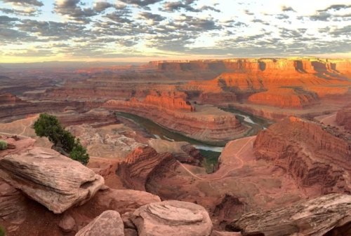 A panoramic view of a canyon at sunset, with layered rock formations and a winding river below.