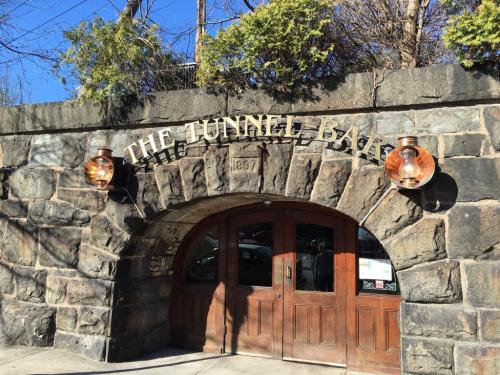 Entrance to The Tunnel Bar, featuring a stone archway and wooden doors, surrounded by greenery and blue sky.