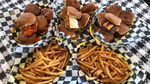 A variety of sliders in baskets with checkered paper, accompanied by golden, crispy French fries.