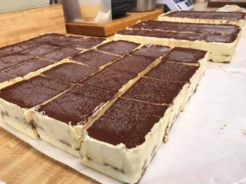 A close-up of neatly cut rectangular slices of layered dessert with a chocolate topping on a wooden surface.