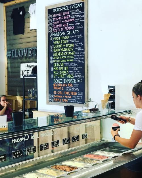 A menu board lists various dairy-free and vegan ice cream flavors at an ice cream shop, with a server preparing an order.