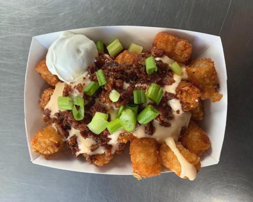 A serving of loaded tater tots topped with cheese sauce, bacon bits, green onions, and a dollop of sour cream.