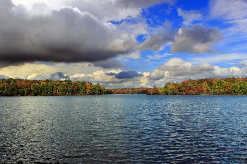 A serene lake surrounded by colorful autumn trees under a dramatic sky with clouds.