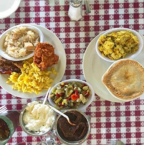 A table set with two plates of comfort food, including fried chicken, noodles, stuffing, salad, and a pie.