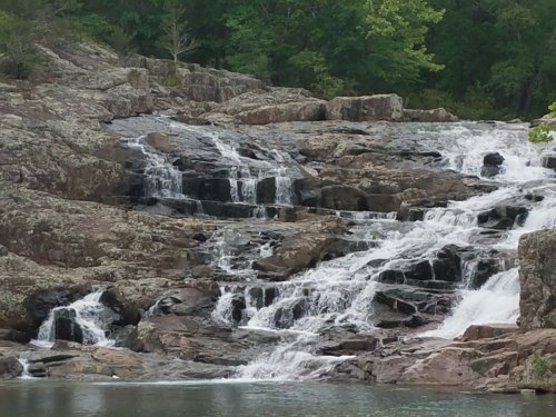 A serene waterfall cascading over rocky terrain, surrounded by lush greenery.