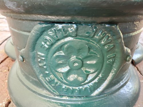 Close-up of a green-painted metal base with embossed floral design and text, resting on a brick surface.