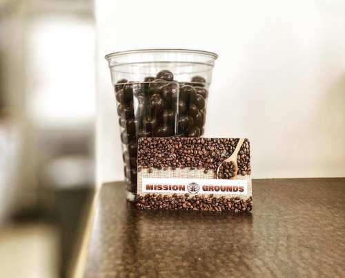 A clear cup filled with dark coffee beans next to a coffee shop loyalty card featuring coffee beans and a spoon.