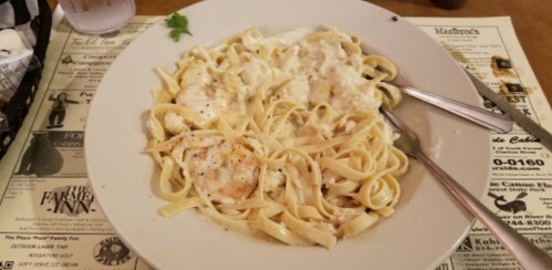A plate of fettuccine pasta topped with creamy sauce and shrimp, served on a restaurant table.