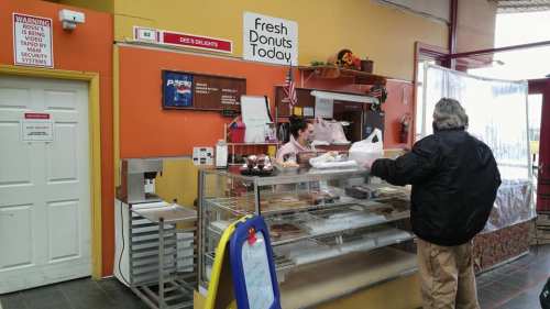 A customer orders donuts at a colorful bakery counter with a sign reading "Fresh Donuts Today."