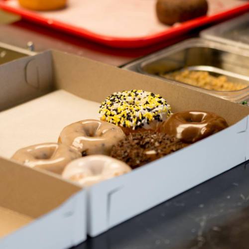 A box of assorted donuts, including glazed, chocolate, and sprinkles, on a countertop.