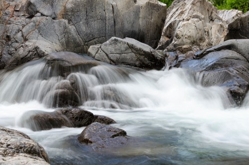 A serene river flows over smooth rocks, creating gentle whitewater cascades amidst rugged stone formations.
