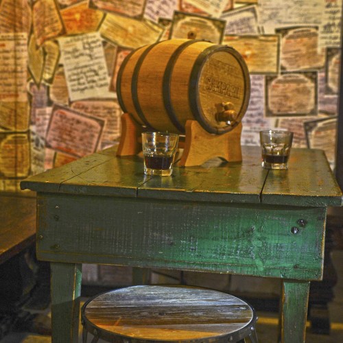 A rustic wooden table with a barrel and two glasses on top, set against a wall covered in handwritten notes.