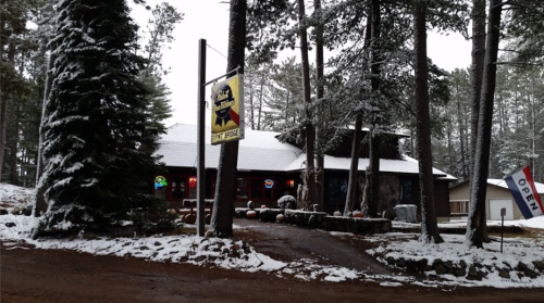 A cozy stone building surrounded by snow-covered trees, with a sign indicating it's open for business.