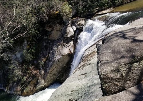 A waterfall cascading over rocky terrain, surrounded by lush greenery and flowing water.