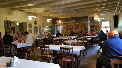 A cozy restaurant interior with wooden tables, patrons dining, and a colorful mural on the wall.