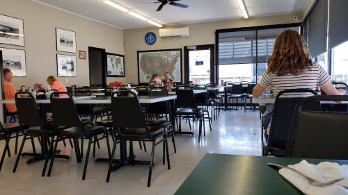 A spacious, mostly empty dining area with tables, chairs, and a map on the wall. A few patrons are seated.