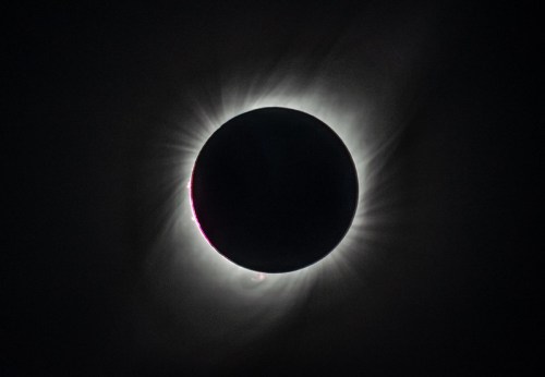 A solar eclipse with a darkened sun surrounded by a glowing corona and rays of light extending outward.