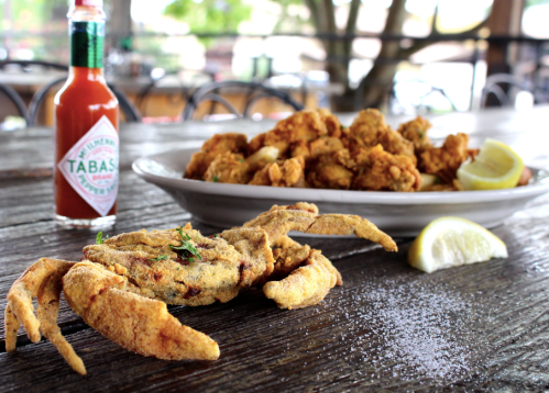 A plate of fried seafood, including a whole crab and fried shrimp, with a bottle of Tabasco sauce and lemon wedges.